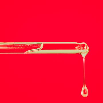 close up of glass pipette with drop of essential oil or face serum on red background trendy products of the year health and wellness concept cosmetic banner with copy space